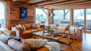 L’intérieur chaleureux d’un chalet, avec un revêtement mural en bois, des canapés en cuir, une table basse en bois et de grandes fenêtres offrant une vue sur l’extérieur.