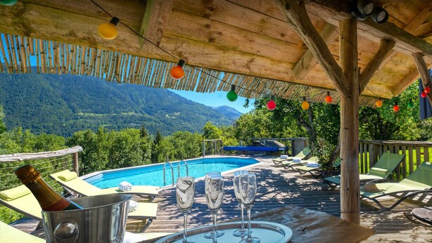 Une terrasse en bois avec une piscine, des chaises longues et une table avec des verres à vin et une bouteille.