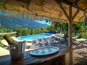 Eine Holzterrasse mit Pool, Liegestühlen und einem Tisch mit Weingläsern und einer Weinflasche.