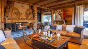 L’intérieur chaleureux d’un chalet avec une cheminée, des canapés en cuir, des tables en bois et un manteau de cheminée en pierre.