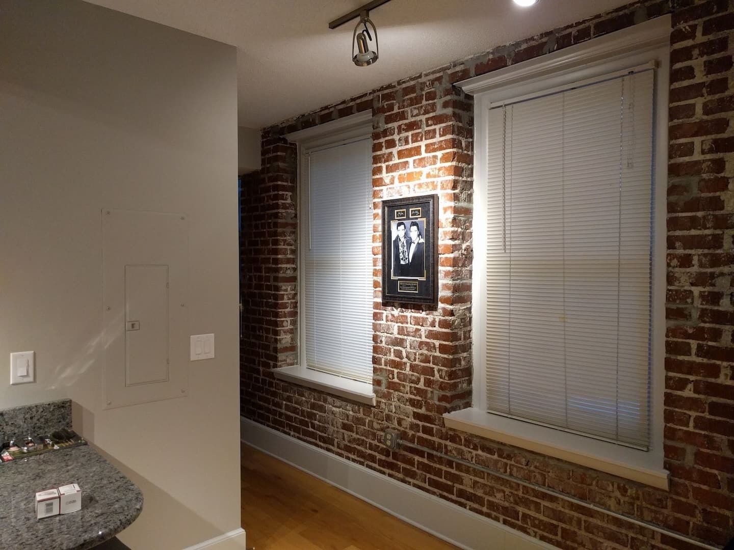 A hallway with brick walls, white-framed windows, and a framed photo on the wall.