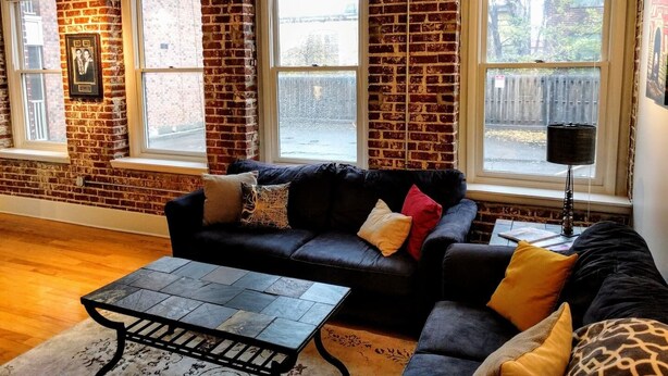 Un salon avec un mur en briques, un canapé en cuir noir, une table basse et un lampadaire.