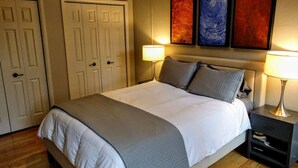 Une chambre d’hôtel avec un lit, deux tables de chevet, une commode et une porte.