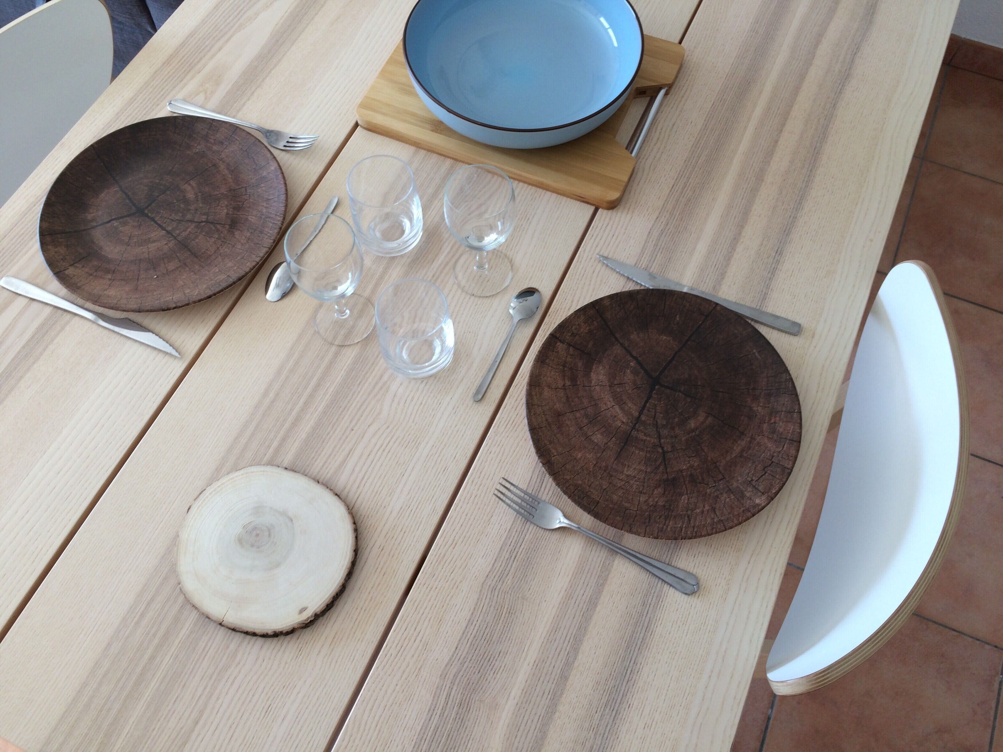 Una mesa de madera con platos, cubiertos y vasos dispuestos para una comida.