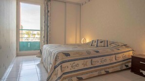 A bedroom with a bed, a window with curtains, a bedside table, and a view of the outside. - Apartment With Balcony And View On The Port. (Fréjus)