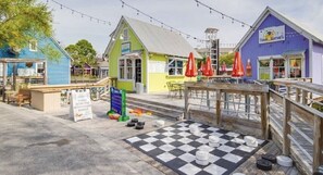 En træpromenade med farverige bygninger, et skakternet område og udendørs siddepladser.