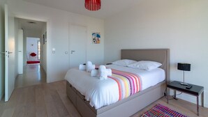 A bedroom with a bed, a bedside table with a lamp, a red pendant light, a colorful rug, and a door leading to another room. - Apartment In A Residence With Swimming Pool Wifi (Cannes)