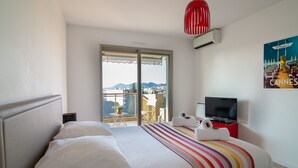 A hotel room with a bed, a TV, a red pendant light, and a poster of Cannes. - Apartment In A Residence With Swimming Pool Wifi (Cannes)