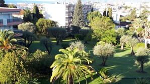 A residential area with a well-maintained lawn, various trees, and a view of a cityscape in the background. - Apartment In A Residence With Swimming Pool Wifi (Cannes)
