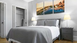 A bedroom with a bed, two bedside lamps, a nightstand, a closet, and a wall with three paintings.