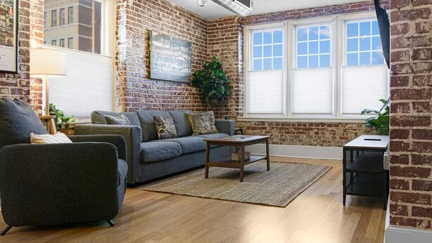 A living room with a brick wall, a grey sofa, a coffee table, and a wooden floor.