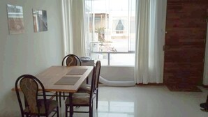 Un comedor con una mesa y sillas de madera, un ventanal con cortinas y vistas al exterior.