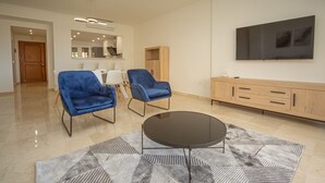 A modern living room with a round coffee table, two blue armchairs, a wooden cabinet, and a flat-screen TV mounted on the wall.