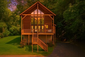 A wooden cabin with a balcony, a staircase, and a view of the surrounding forest.