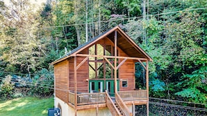 Uma cabana de madeira com varanda e escadas, rodeada por uma floresta densa.