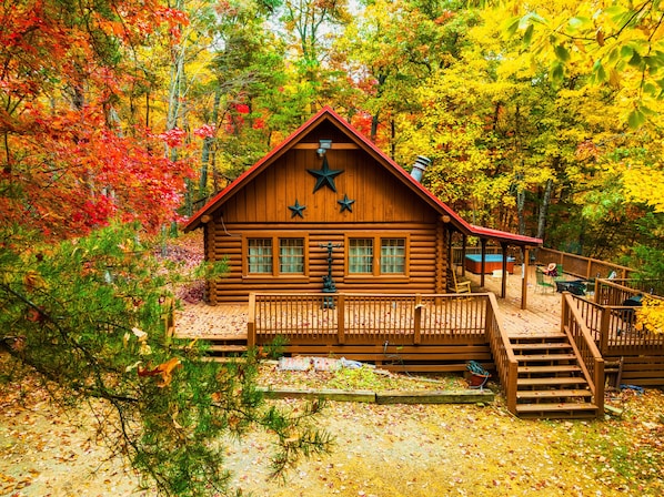 Situated in a forested area, this cabin features a wooden deck and stairs leading to its entrance.