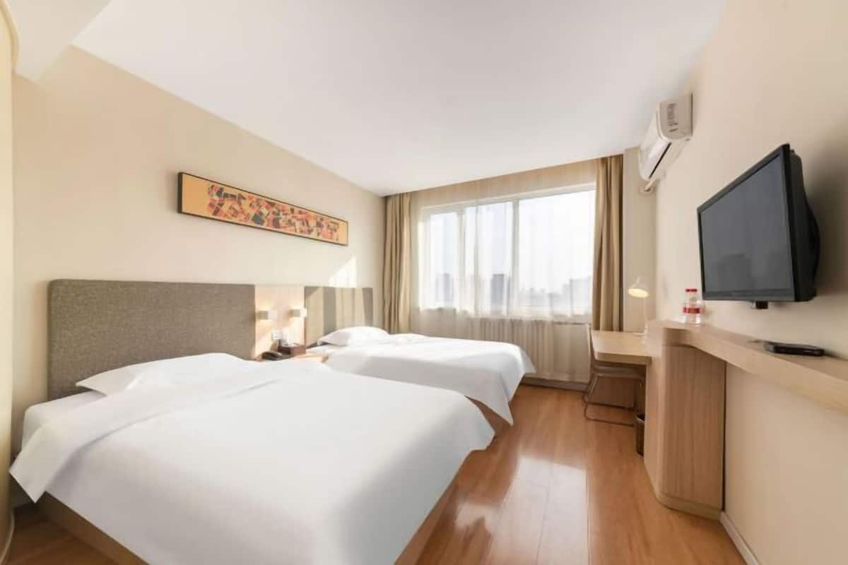 A hotel room with two beds, a TV, a desk, and a window with curtains.