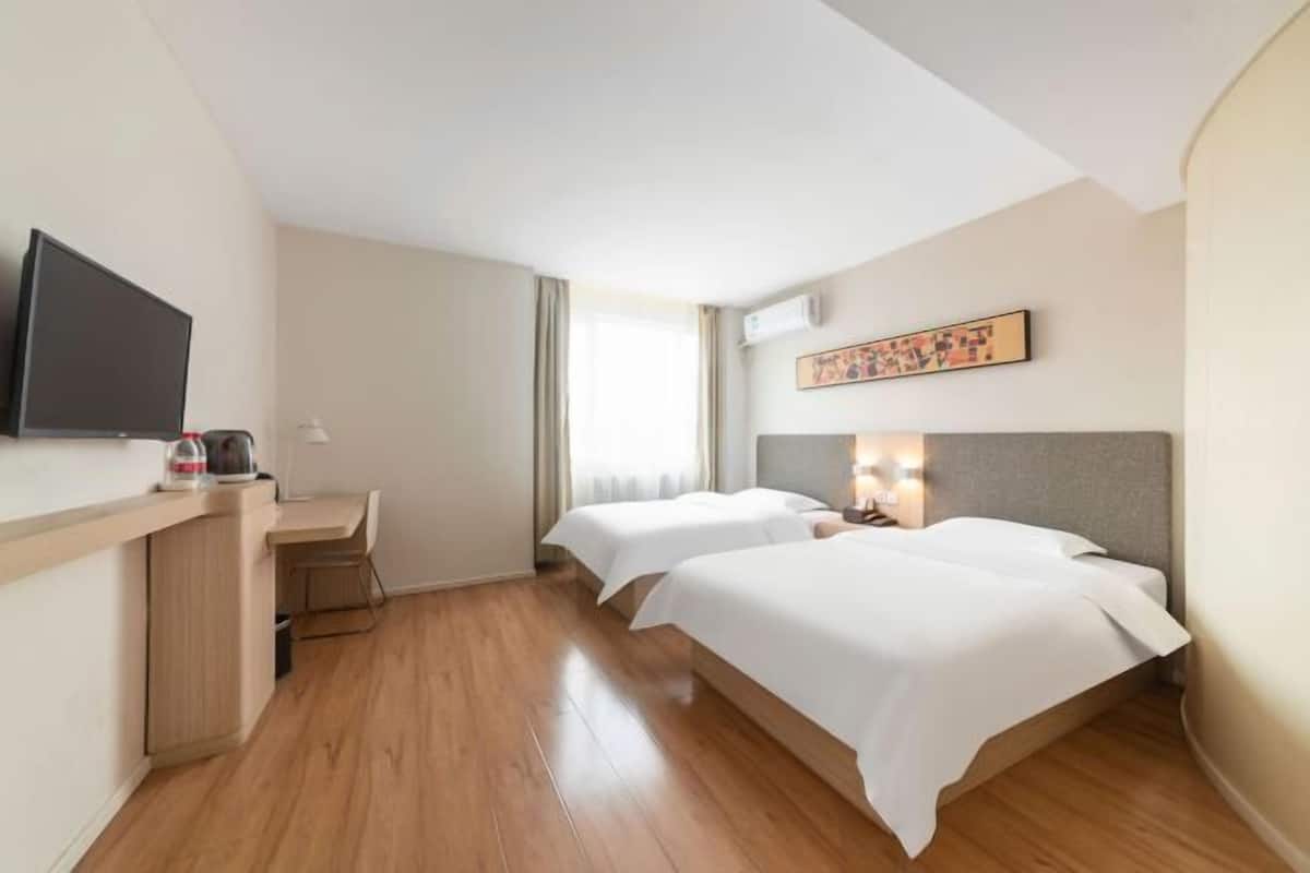 A hotel room with two beds, a desk, a flat-screen TV, and a painting on the wall.