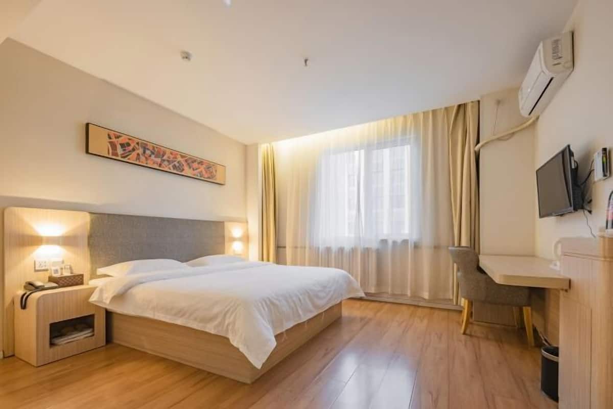 A hotel room with a bed, bedside table, lamp, desk, chair, and a TV.