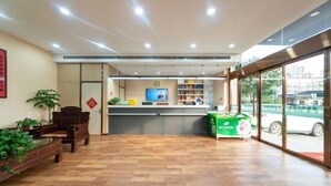 A reception area with a wooden floor, a reception desk, a green counter, and a large window with a view of the outside. - Lianjia Holiday Hotel (Jigang Senior High School) (Jinan)