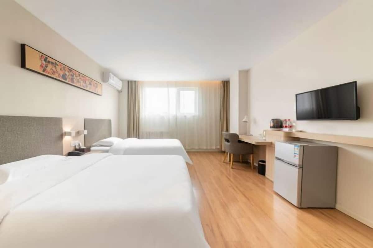 A hotel room with two beds, a desk, a television, and a refrigerator.