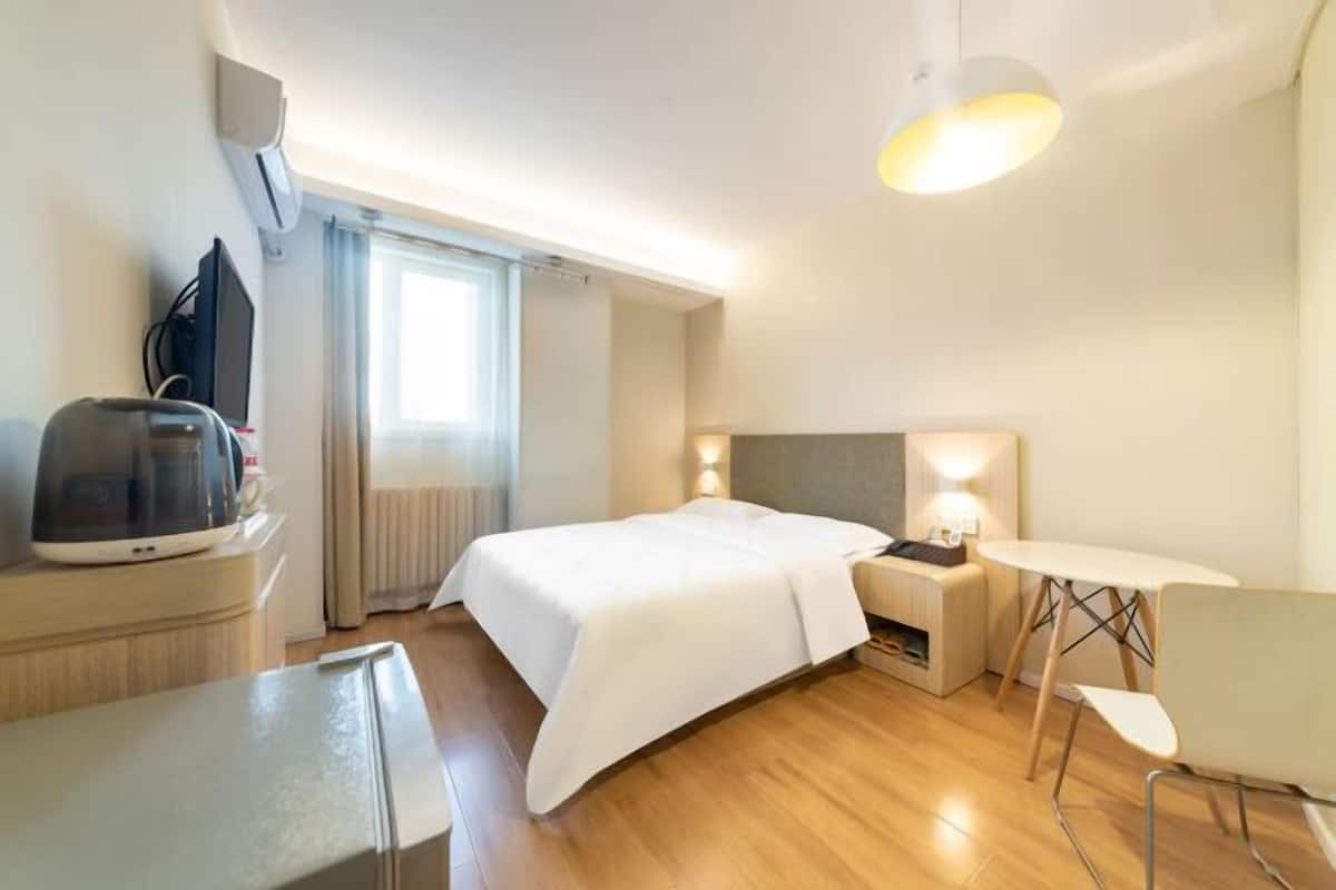 A hotel room with a bed, bedside table, lamp, and a small table with a chair.