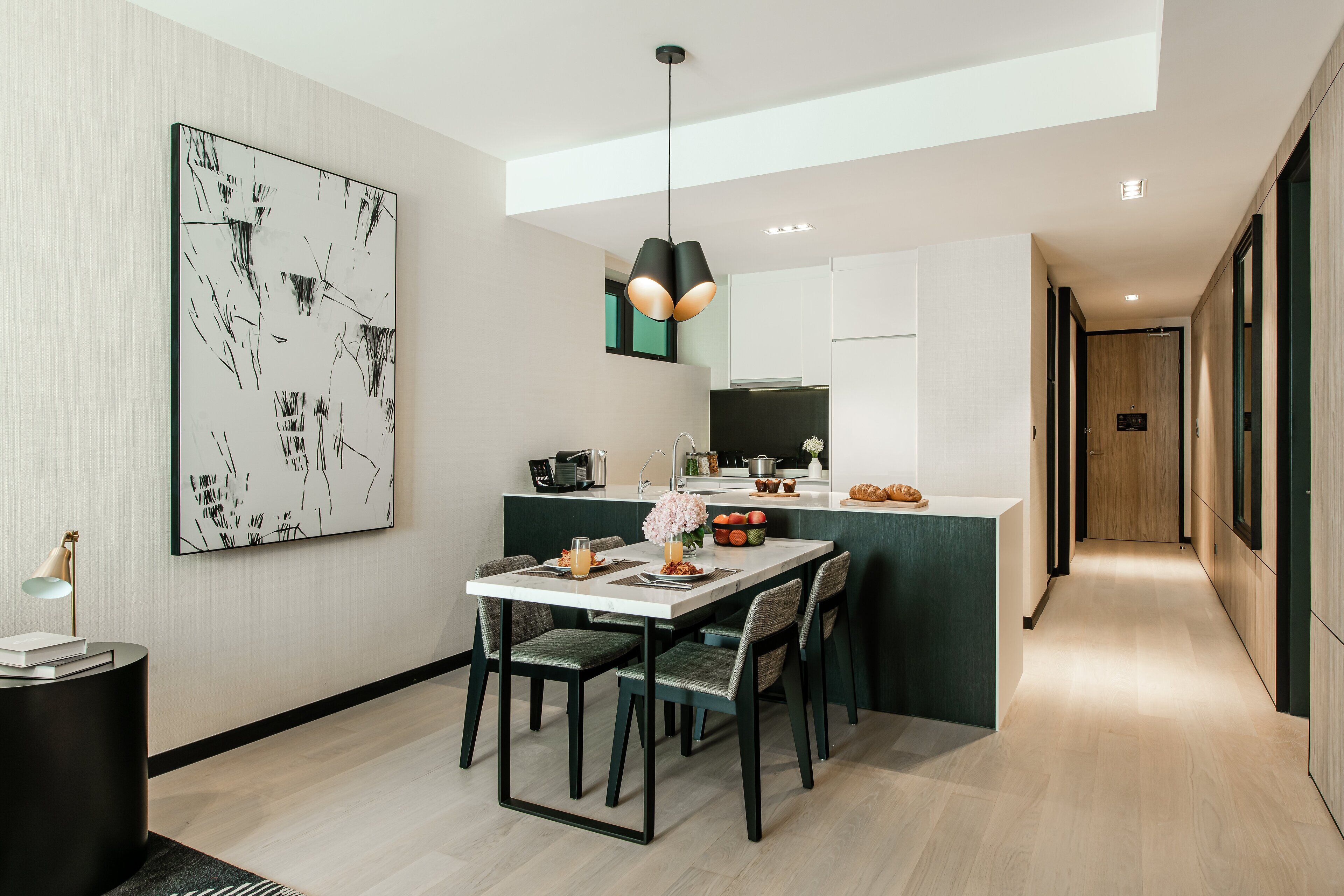 A modern kitchen with a dining area, featuring a central island, pendant lighting, and a large abstract painting on the wall.