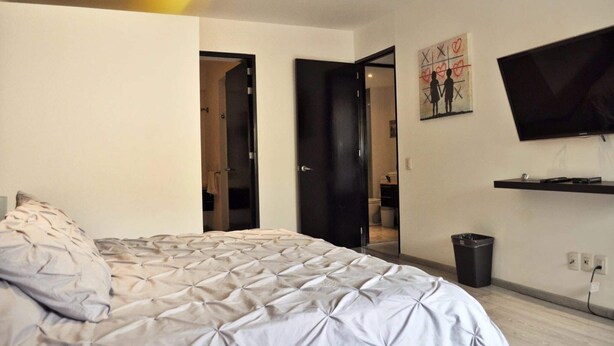 Une chambre à coucher avec un lit, un téléviseur fixé au mur et une porte donnant sur une autre pièce.
