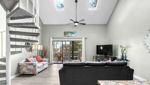 A spacious living area with a grey sofa, a wooden coffee table, a TV, and a staircase with a unique design. - Rudy's Reel 'Em Inn By Beach Star (Myrtle Beach)