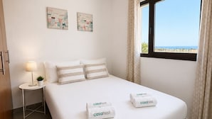 Ein Hotelzimmer mit einem Bett, zwei Wandbildern, einem Nachttisch mit Lampe und einem Fenster mit Vorhängen.