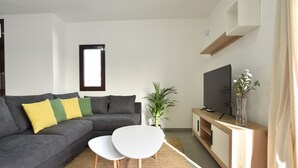 Ein modernes Wohnzimmer mit einem grauen Sofa, einem weißen Couchtisch, einem Fernseher auf einem Holzboden und einer Topfpflanze.