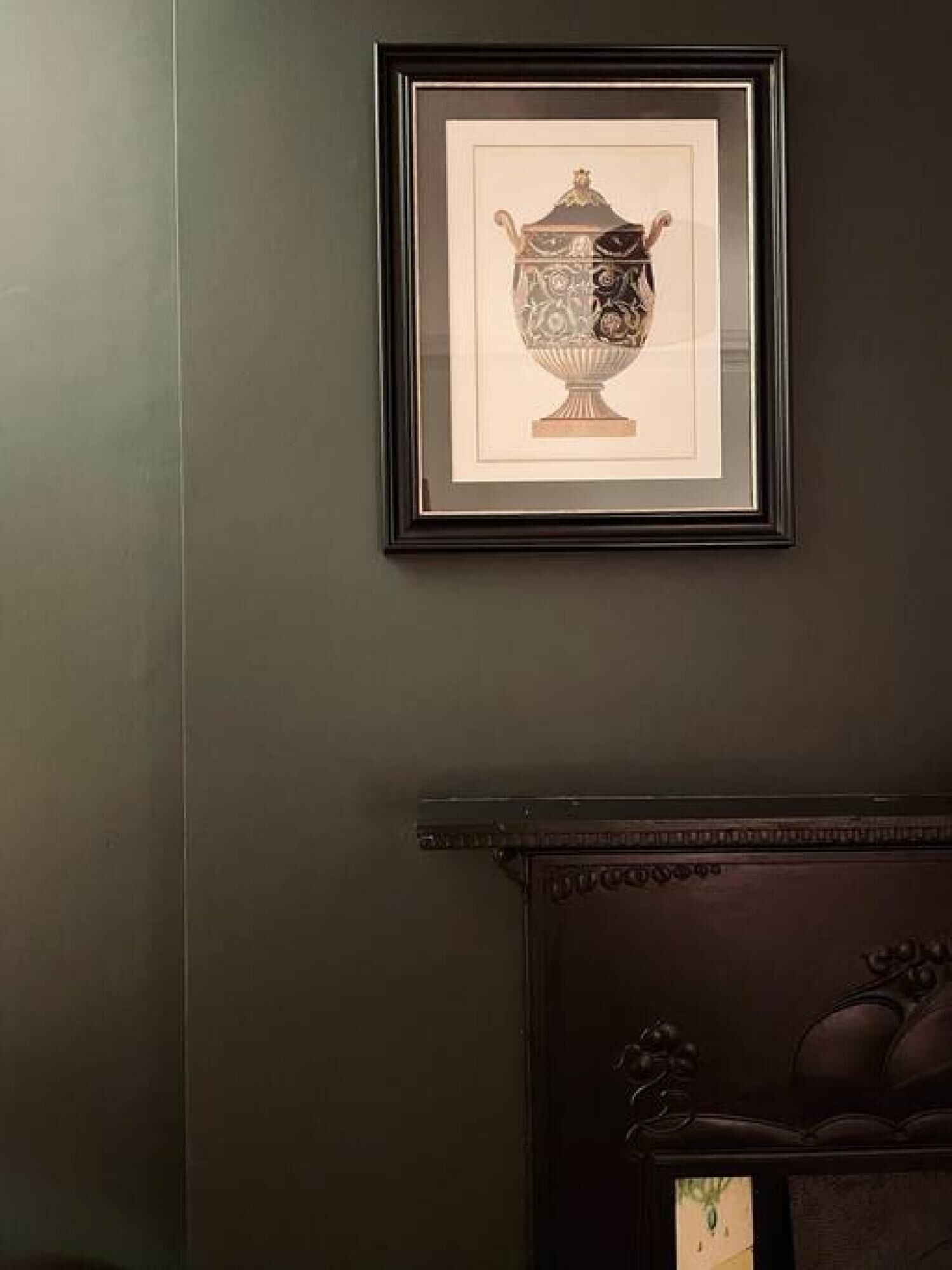 Une œuvre d’art encadrée représentant un vase décoratif sur un mur sombre.