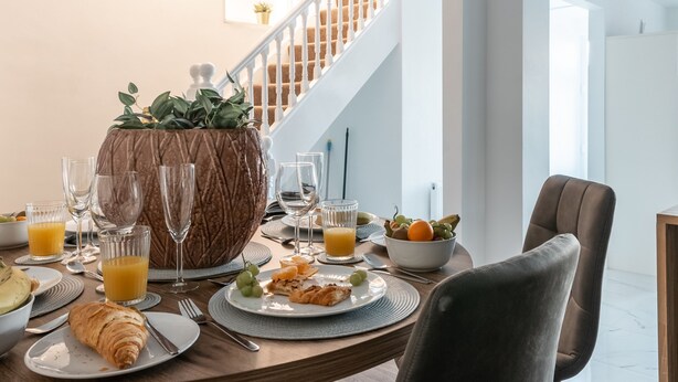 Comedor con una mesa de madera preparada para el desayuno, con croissants, fruta y vasos de zumo de naranja.