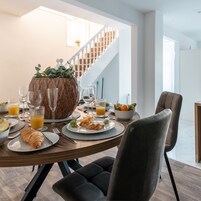 A dining area with a wooden table set for breakfast, including croissants, fruit, and orange juice glasses.