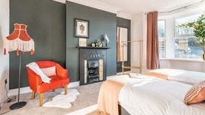 Un dormitorio moderno con chimenea, un sillón rojo, dos camas y vistas de la ciudad a través de una ventana.