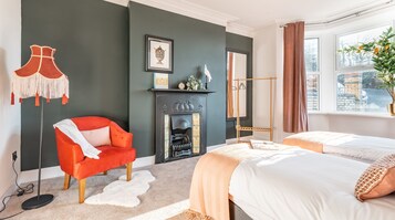 A modern bedroom with a fireplace, a red armchair, two beds, and a view of the city through a window.