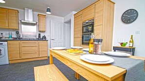 A modern kitchen with wooden cabinets, a stainless steel range hood, and a dining area with a bench and table set for two.