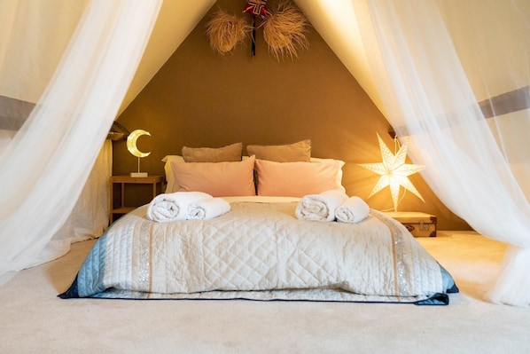 A cozy, triangular tent-style bedroom with a bed, pillows, and two decorative lights.
