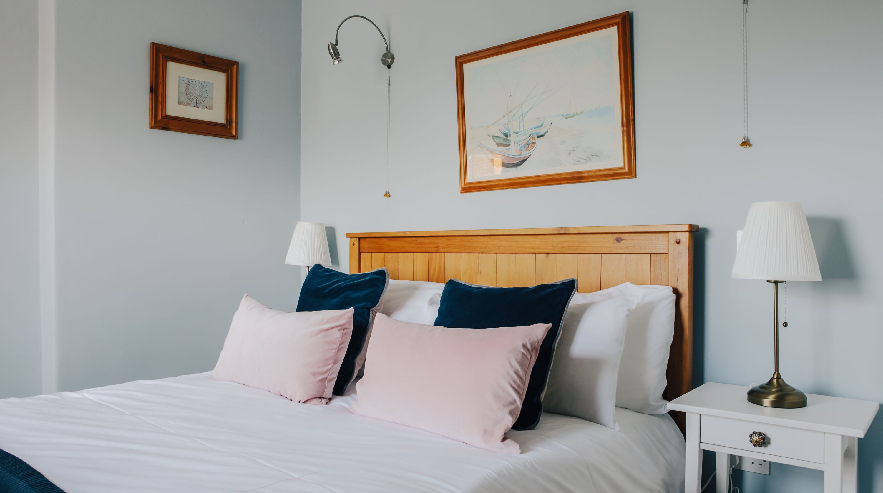 Un lit bien fait, avec une tête de lit en bois, deux tables de chevet avec des lampes et un tableau encadré accroché au mur.