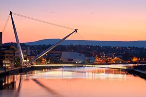 A bridge with a cable structure over a calm river, reflecting lights, with a cityscape in the background. - Eveswell Studios Comfort Studio 10 (Newport)