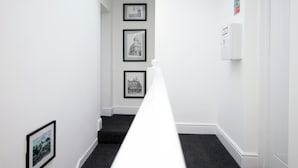 A narrow hallway with black carpet, white walls, and framed black-and-white photographs on the walls. - Eveswell Studios Comfort Studio 10 (Newport)