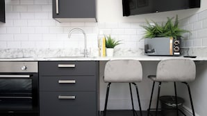 A modern kitchen with a built-in oven, a sink, and two bar stools. - Eveswell Studios Comfort Studio 10 (Newport)