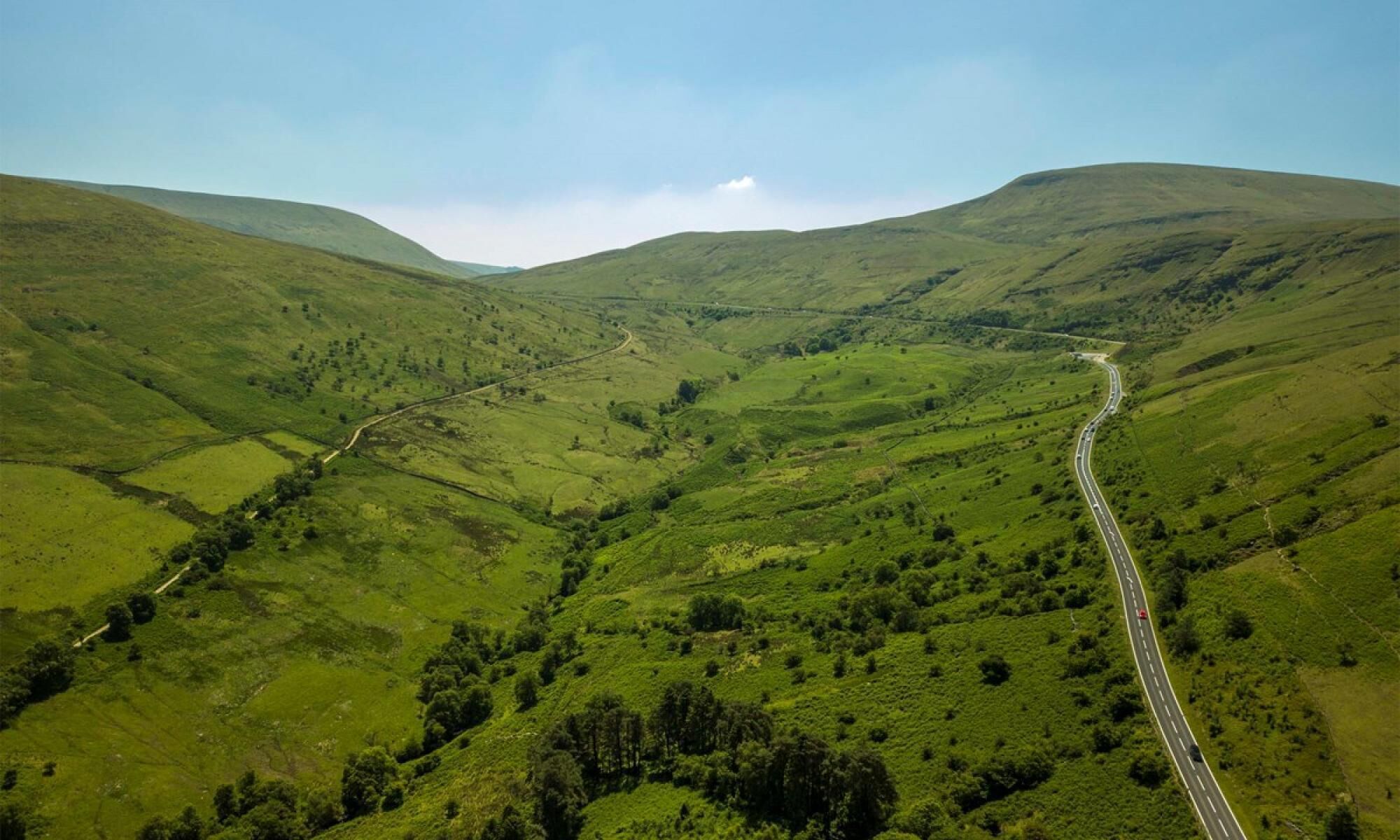 A winding road through a valley with lush green hills and sparse trees.