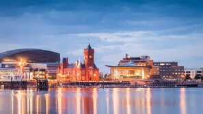 A waterfront cityscape with a prominent red building with a clock tower, a modern structure with a curved roof, and a large stadium.