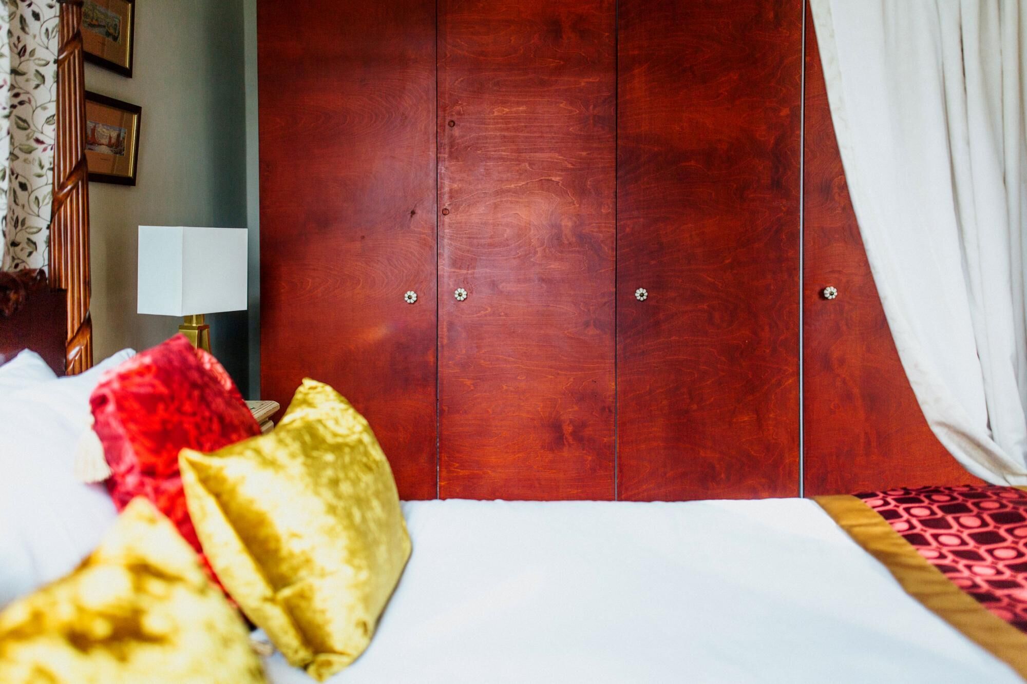 Een hotelkamer met een houten garderobe, een bed met witte beddengoed en een gestreept plaids.
