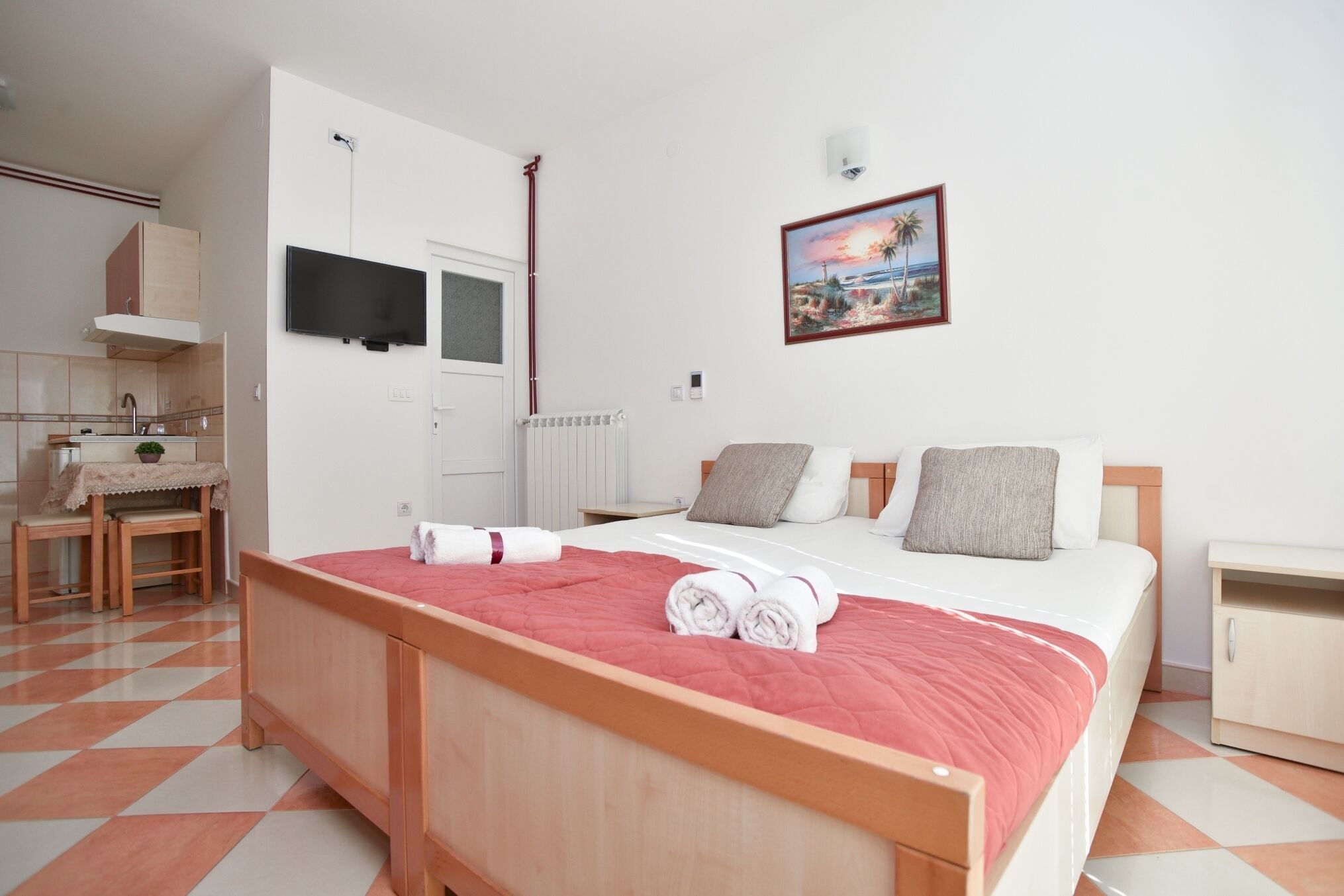 Een slaapkamer met een bed, nachtkastje, raam, schilderij, stoel, tafel en een wastafel.