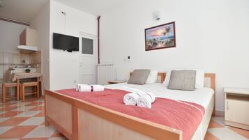 Een slaapkamer met een bed, nachtkastje, raam, schilderij, stoel, tafel en een wastafel.