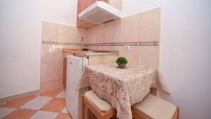 Eine kompakte Küche mit Kühlschrank, Spüle und einem kleinen Tisch mit Spitzenleinentuch und einer Topfpflanze.