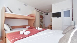 Ein Hotelzimmer mit einem Etagenbett, einem großen Bett mit roter Decke, einem an der Wand befestigten Fernseher und einer Tür zu einem Badezimmer.