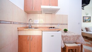 Eine kleine Küche mit Holzausstattung, integriertem Spülbecken, einem weißen Kühlschrank und einem Tisch mit Spitzenbettdecke.